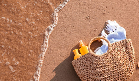 Rantakassi jossa aurinkosuojavoiteita rantahiekalla, taustalla  n&auml;kyy meren aaltoja