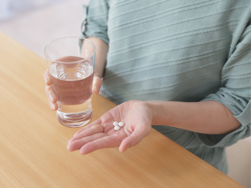 Nainen vesilasi k&auml;dess&auml; ja  pillereit&auml; k&auml;dess&auml;