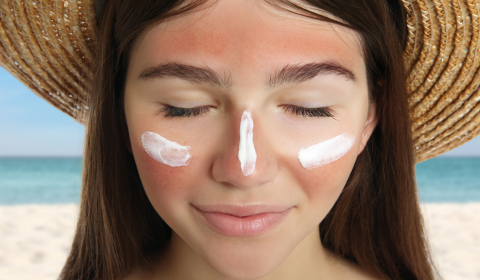 Nainen aurinkohattu p&auml;&auml;ss&auml; ja aurinkorasvaa poskilla je nen&auml;np&auml;&auml;ss&auml;