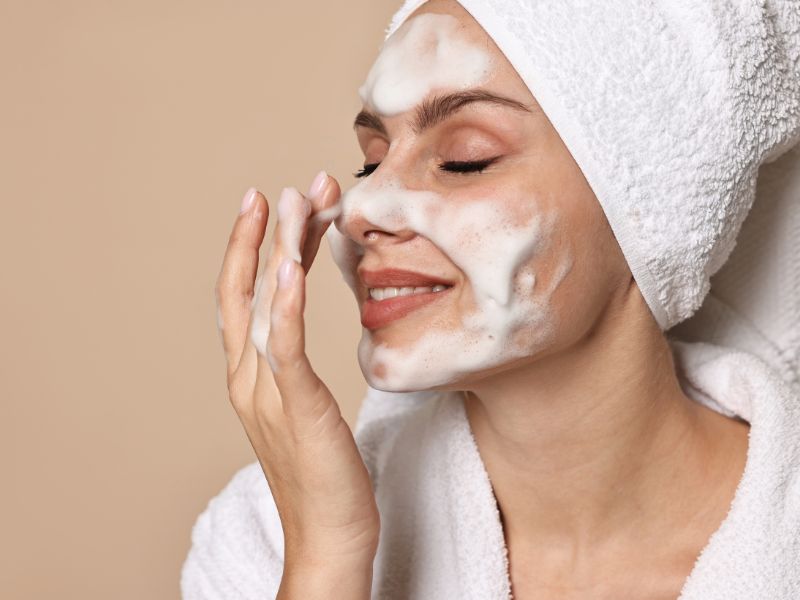 Naisella vaahtoa kasvoilla ja pyyhe hiuksissa. On pesem&auml;ss&auml; kasvojaan