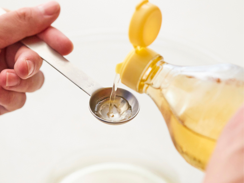 Mies kaataa pullosta kullankeltaista &ouml;ljy&auml; lusikkaan